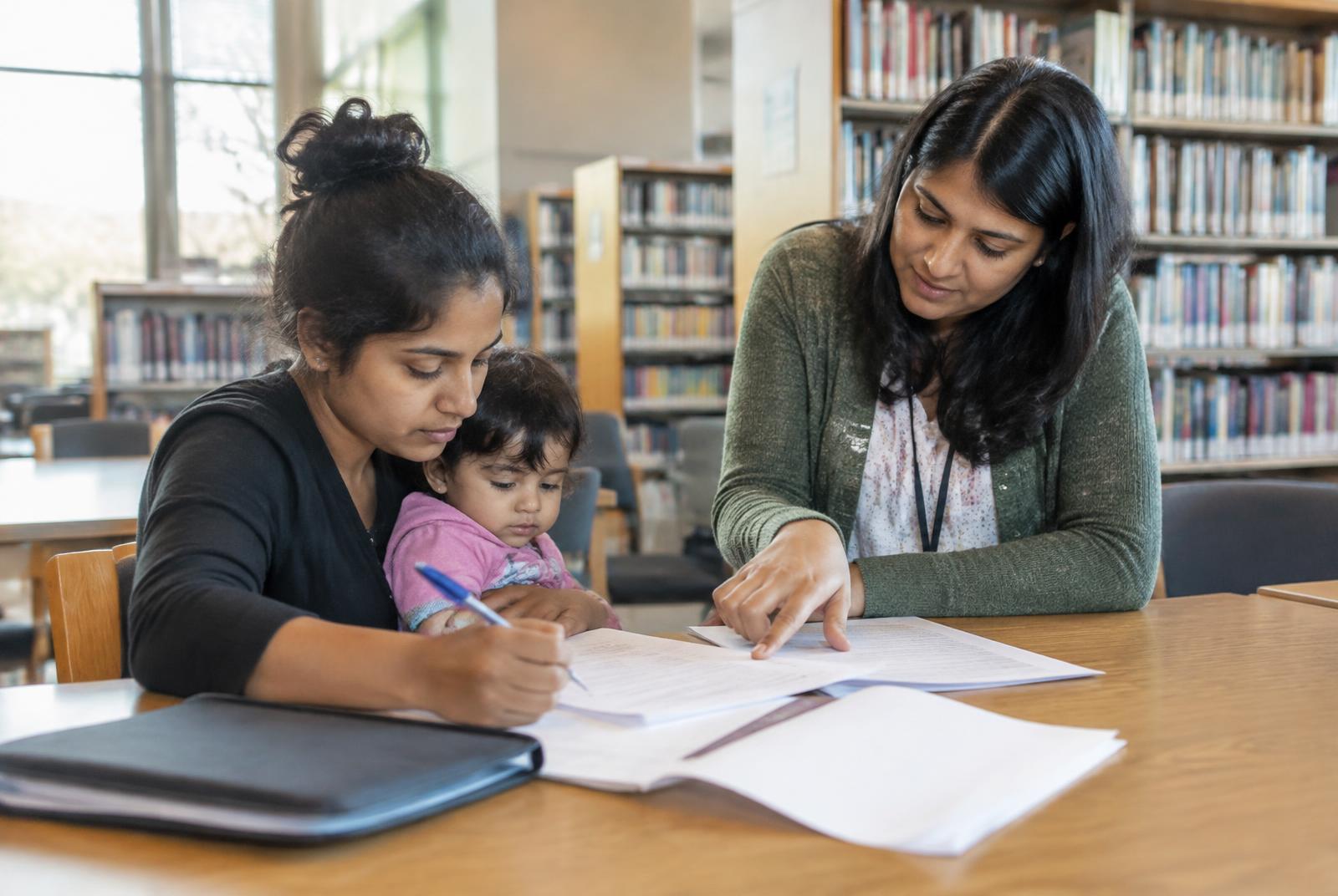 A legal volunteer helping a mother understand forms at a public library